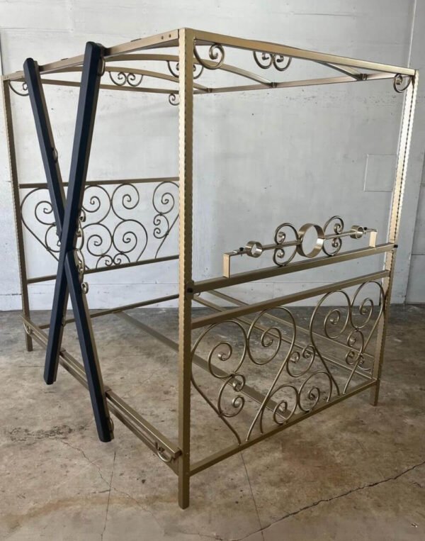 The Scroll Bed in Spanish Gold with Stockade by Metalbound: an ornate metal bed frame with intricate scrollwork, finished in luxurious Spanish gold, featuring an integrated stockade for versatile and secure bondage play.